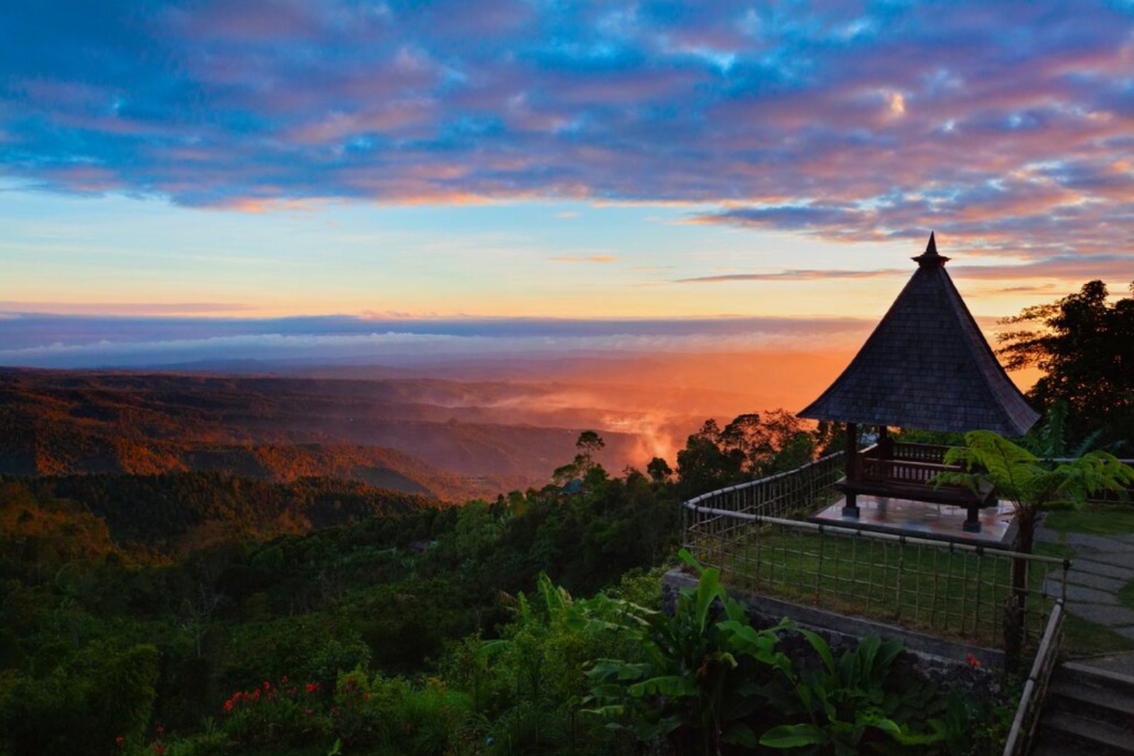 Sunrise over the Munduk highlands in North Bali, with a hilltop gazebo overlooking misty forested valleys